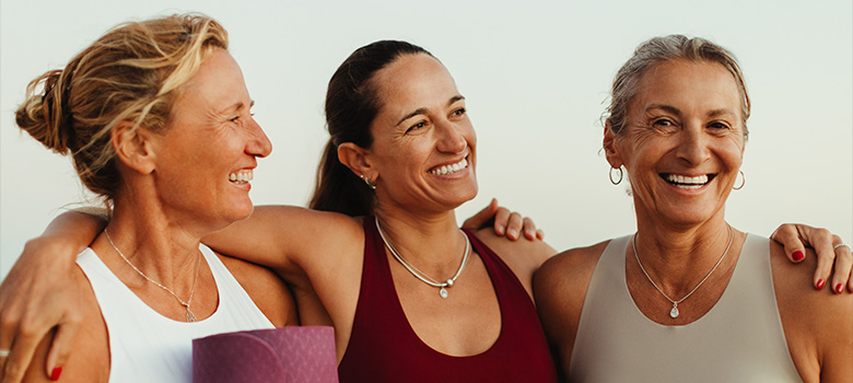 three happy women smiling together wearing athletic clothing in a outdoor setting enjoying fitness and friendship