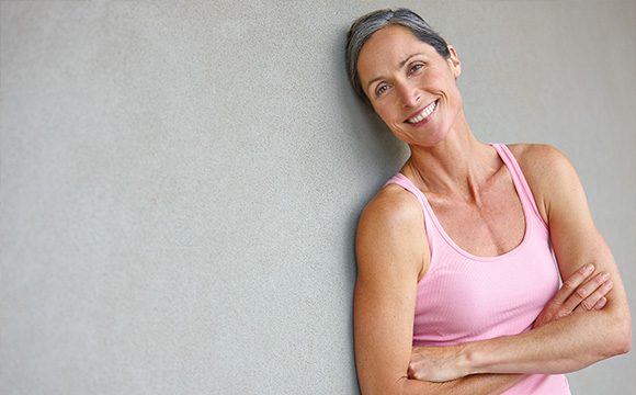 smiling woman in fitness attire standing against a wall displaying confidence and vitality showcasing healthy lifestyle choices from a fitness perspective emphasizing 7 ways to stay fit
