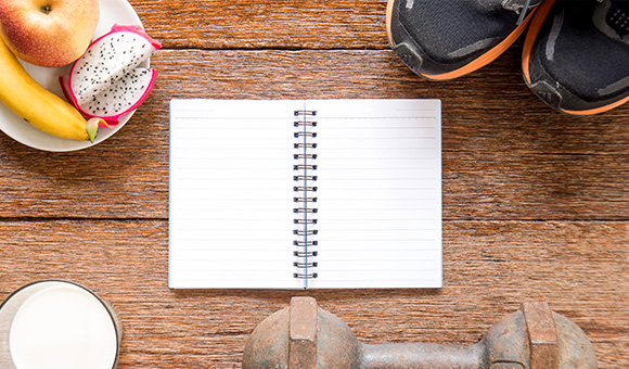 notebook with blank pages surrounded by fresh fruits a banana an apple a dragon fruit a glass of milk a dumbbell and a pair of running shoes designed for a healthy lifestyle and exercise routines with six steps to fitness
