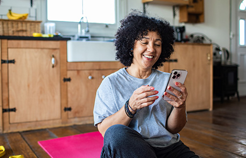 smiling woman sitting on exercise mat using smartphone in home kitchen enjoying online content related to health and wellness 4 simple tips for fitness