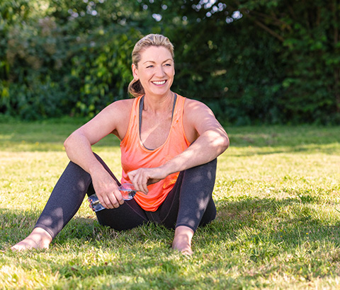 smiling woman in athletic wear sitting on grass holding a water bottle enjoying her fitness routine surrounded by greenery six steps to wellness