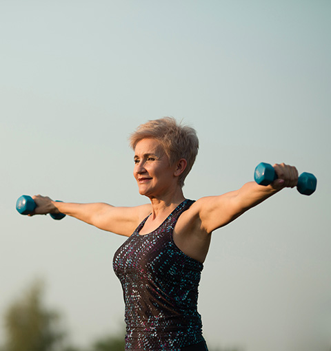 woman exercising with two dumbbells outdoors in fitness attire during sunset