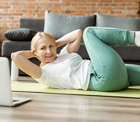 woman exercising with crunches on a yoga mat at home using laptop for guidance fitness routine with two simple moves