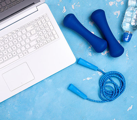 a flat lay of a laptop a pair of blue dumbbells a blue jump rope and a water bottle on a blue background promoting a healthy lifestyle with two fitness tools